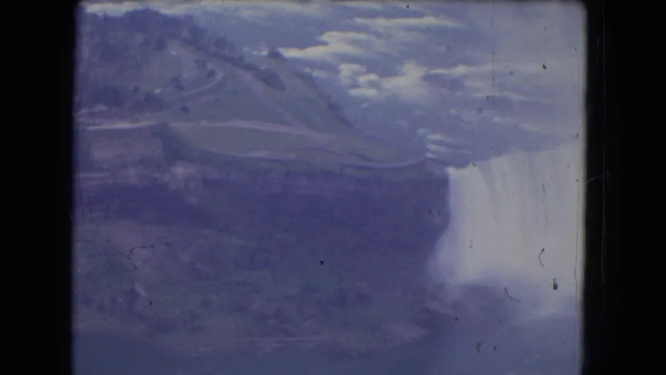 Aerial 8mm frame of Niagara Falls with a bright mist cloud, river edge, and muted surrounding landscape.