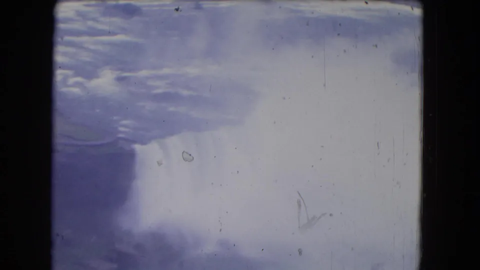 1964 8mm view of Niagara Falls, New York, showing a bright sheet of falling water, mist, soft color, and visible film scratches.