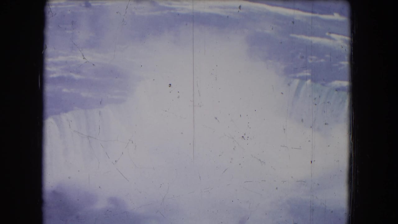 1964 Niagara Falls home-movie frame with a bright mist plume, falling water at the right edge, and visible dust and scratches on the 8mm scan.