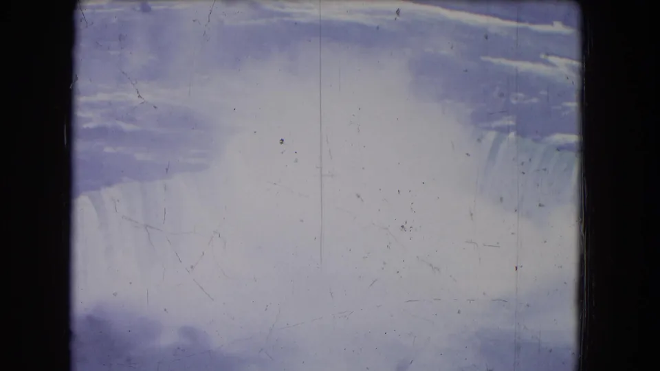 1964 Niagara Falls home-movie frame with a bright mist plume, falling water at the right edge, and visible dust and scratches on the 8mm scan.