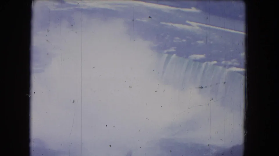 1964 8mm footage of Niagara Falls from an angled viewpoint, showing the waterfall crest, vertical water streaks, dense mist, and faded color.