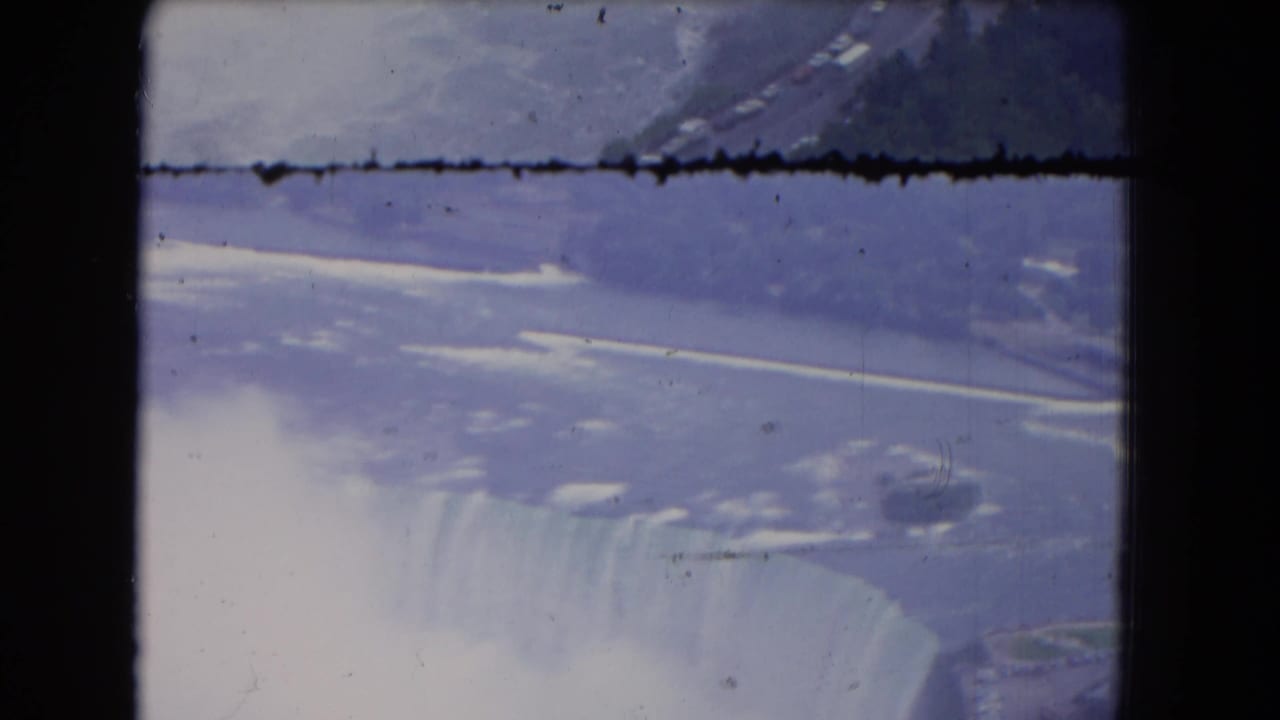 Aerial view across the river toward the waterfall edge, mist, snow or ice, and shoreline.