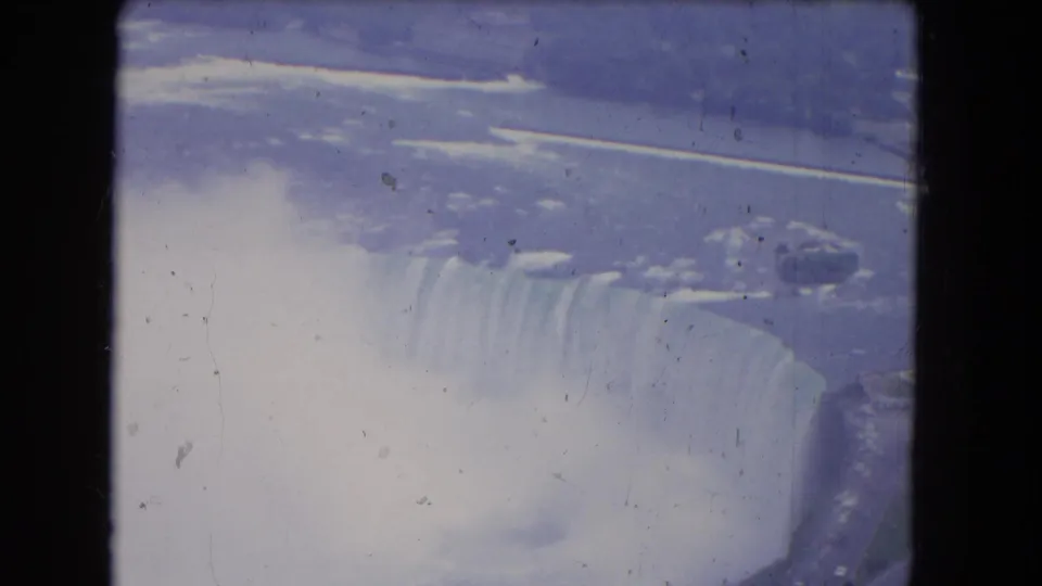 Vintage 8mm aerial view of Niagara Falls in winter conditions, with the cascade partly softened by mist and aged film texture.