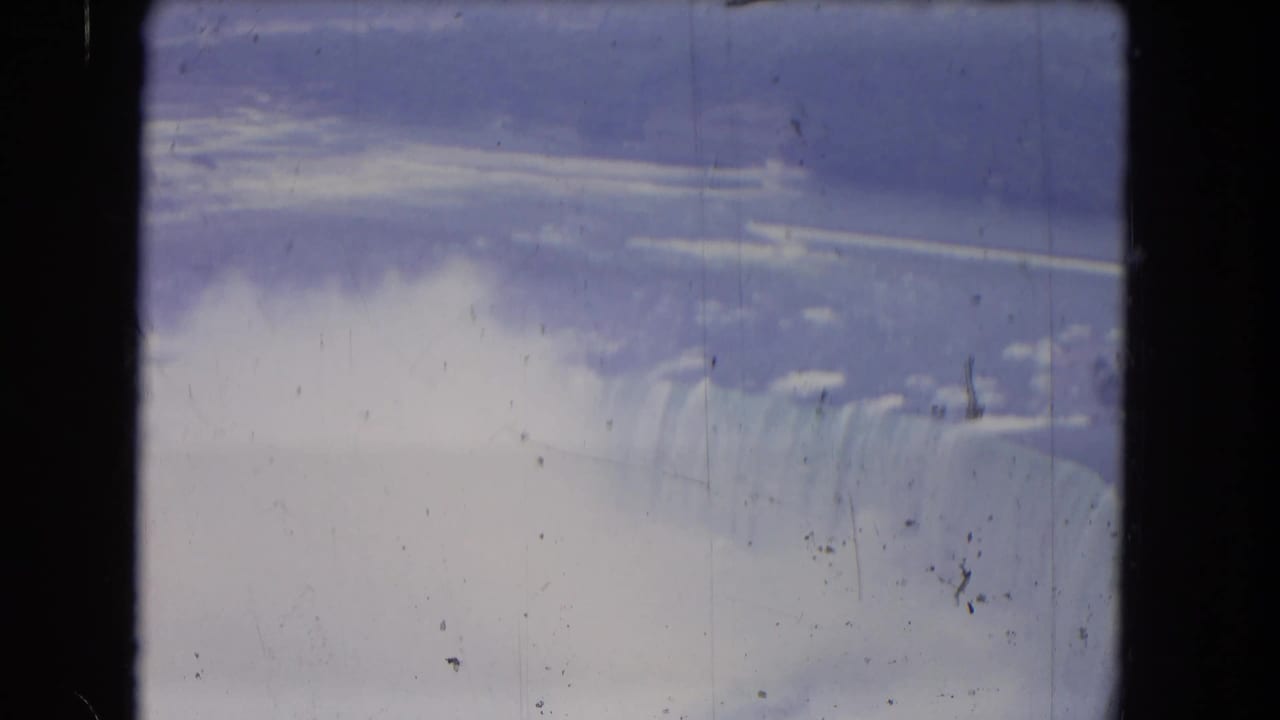 Wide view of Niagara Falls with mist, cloudy sky, and dark film frame edges.