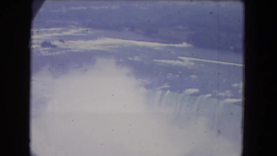 1964 8mm view of Niagara Falls from above, with mist rising behind dark foreground window or support bars.