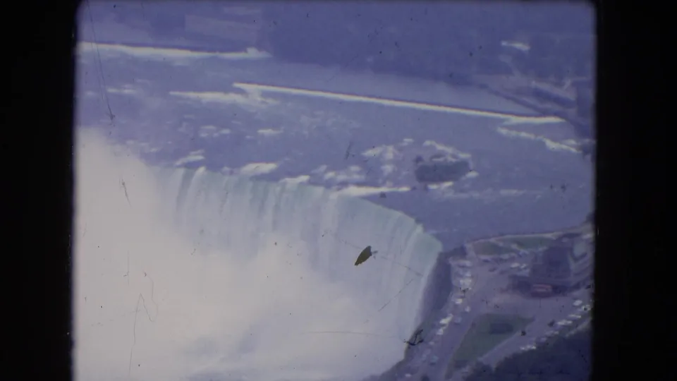 1964 8mm aerial view of Niagara Falls showing Horseshoe Falls, heavy mist, river water, and nearby roads.