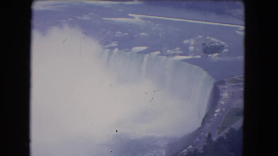 Vintage 8mm frame of Niagara Falls from above, with mist drifting across Horseshoe Falls and roads at the shoreline.