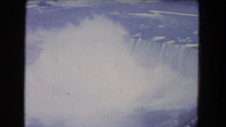 1964 aerial home-movie view of Niagara Falls with heavy mist softening the Horseshoe Falls edge and river below.