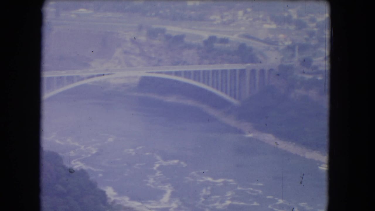 Aerial frame of an arched bridge crossing water with shoreline beyond.