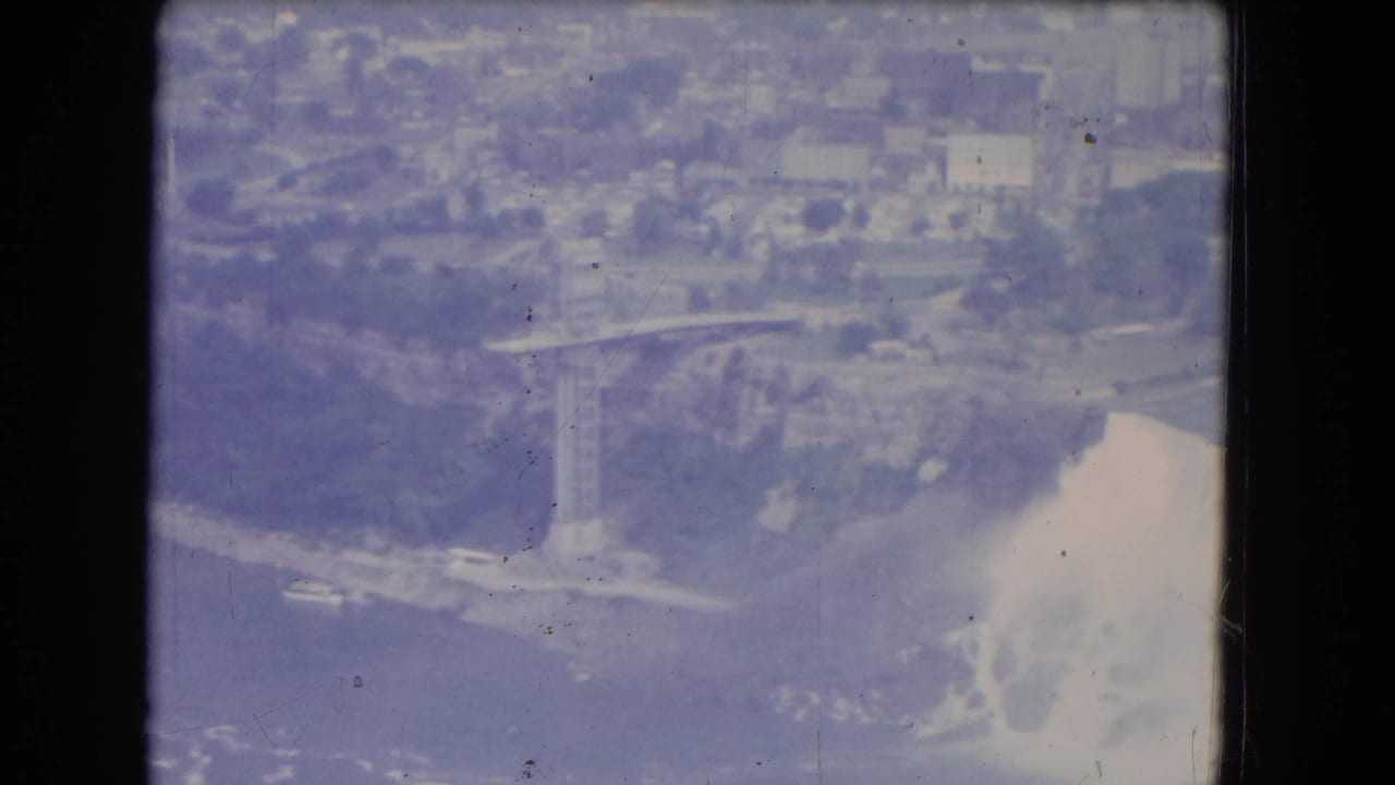 Aerial view of American Falls with mist, river edge, and city buildings beyond.
