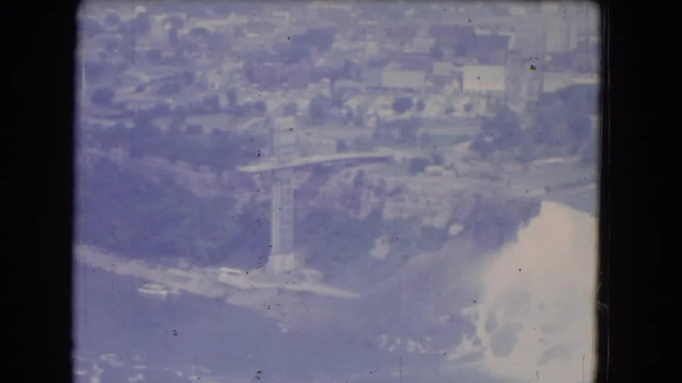 1964 8mm aerial view of American Falls at Niagara Falls, New York, with mist rising below Prospect Point and buildings in the distance.