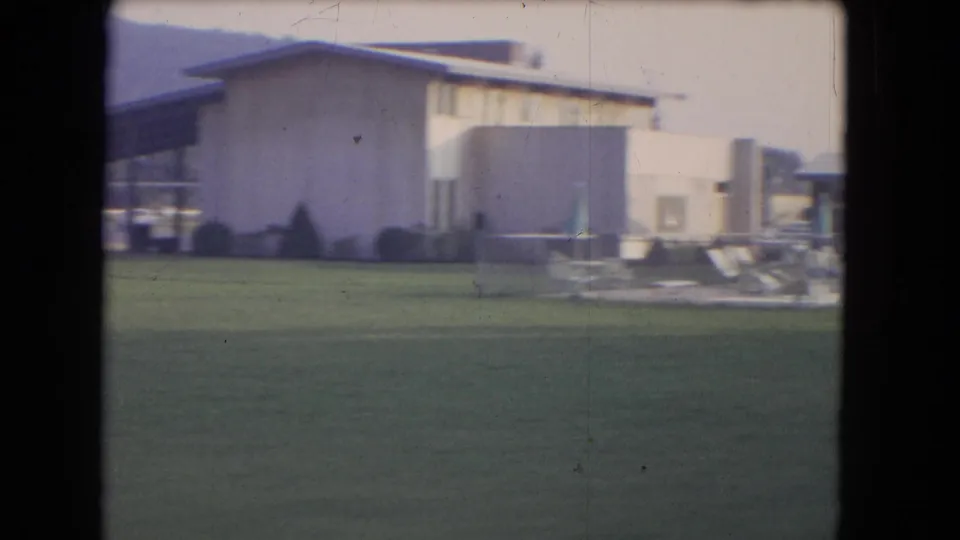 1964 Niagara Falls home-movie frame showing a grassy pool area, low flat-roof building, lounge chairs, and closed umbrellas.