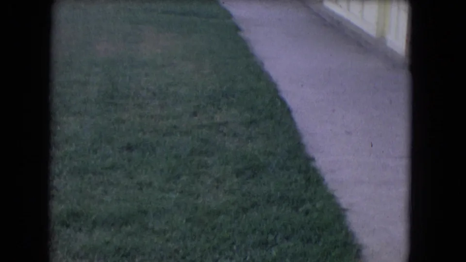 1964 Niagara Falls home-movie frame showing grass and a concrete walkway along the side of a pool building.