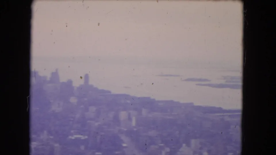 1964 8mm aerial frame with skyline silhouettes, open water, soft focus, and visible aged-film artifacts.