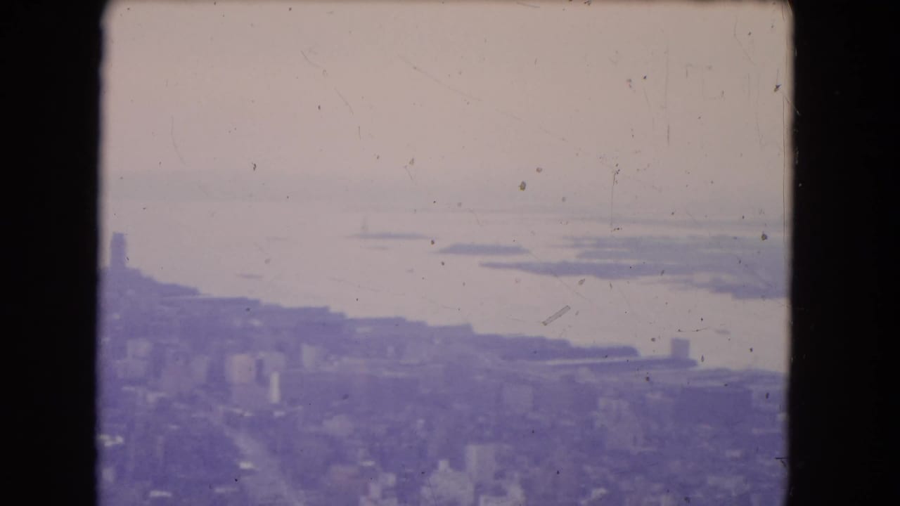 Soft aerial view of waterfront, distant islands, and a hazy city edge.