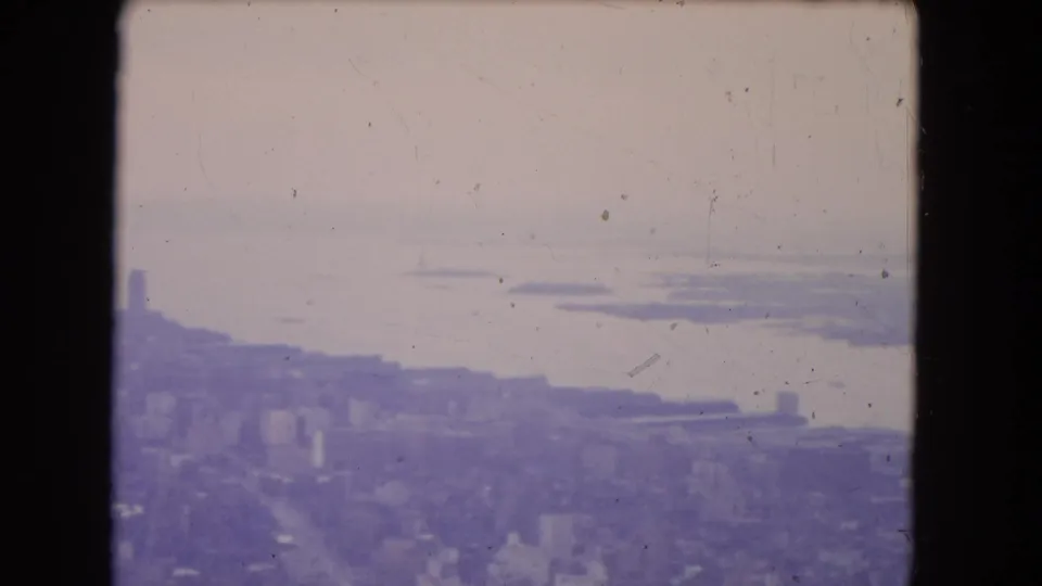 1964 8mm frame showing a hazy aerial view over New York City waterfront and distant landforms, with heavy purple color shift.