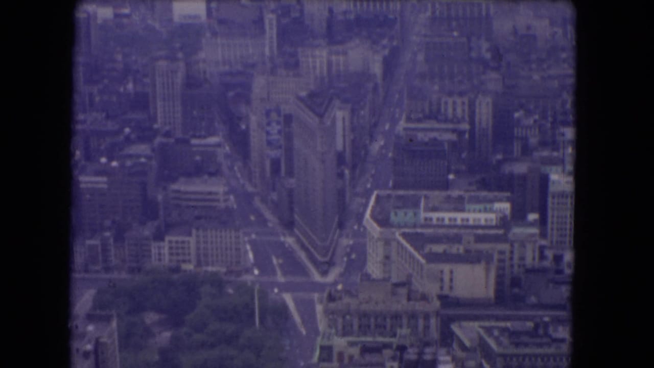 Aerial view over a dense city with a triangular building and broad streets below.