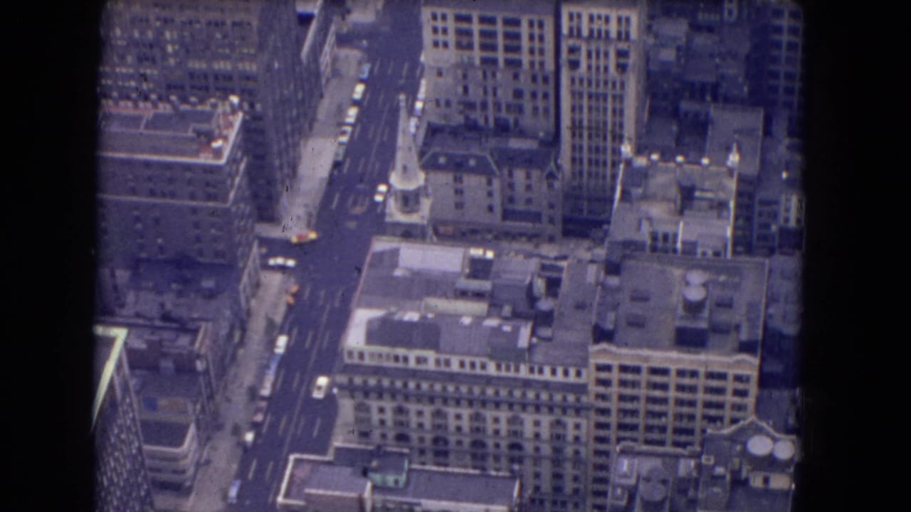 1964 8mm aerial view, likely from Niagara Falls or New York State metadata, showing high-rise buildings, rooftops, streets, and cars below.