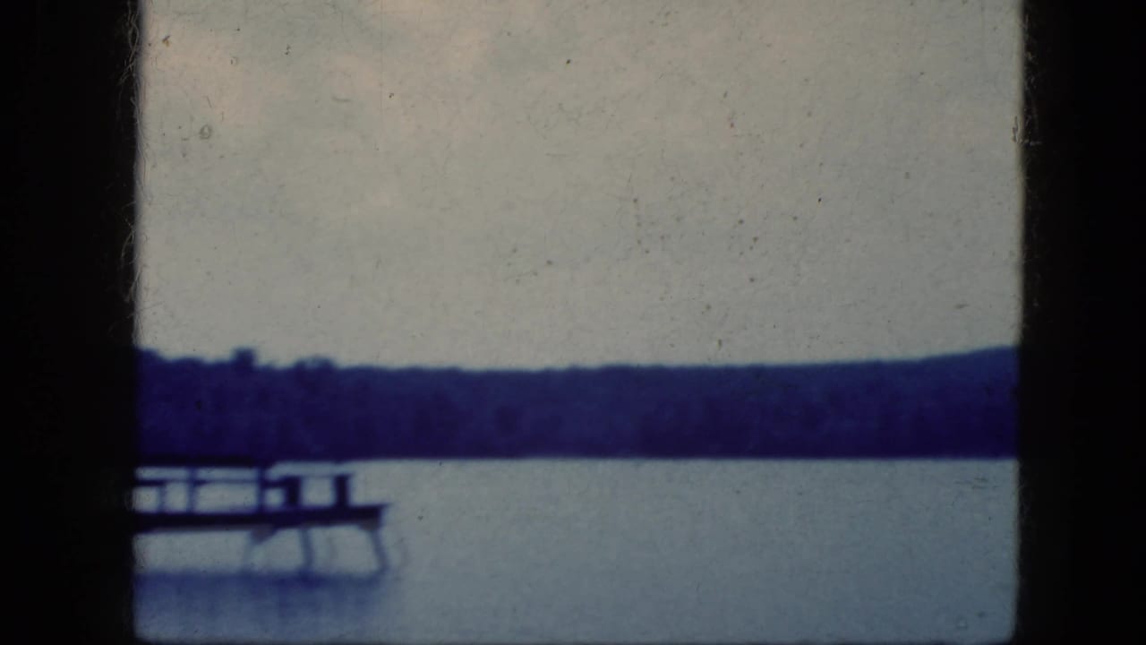 Wooden dock on a lake with a small boat nearby and trees across the water.