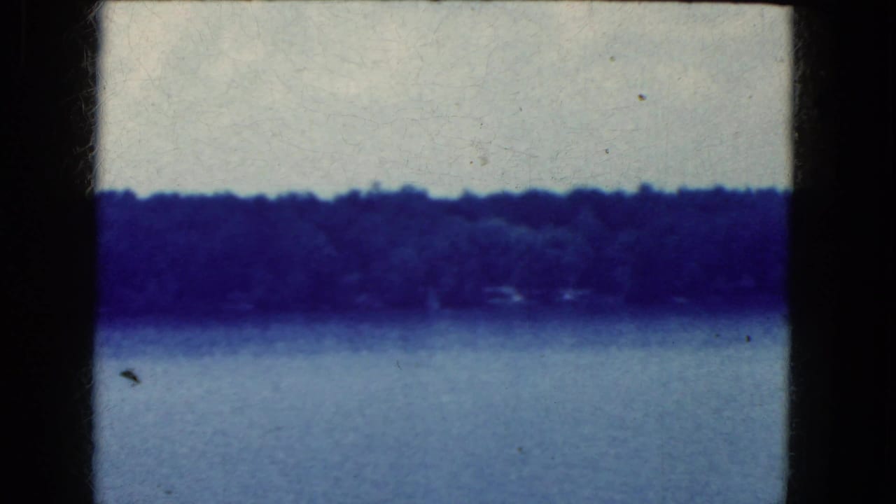 Blue-tinted 8mm frame of water and a far wooded shoreline near Niagara Falls, with soft focus, dust specks, and dark film edges.
