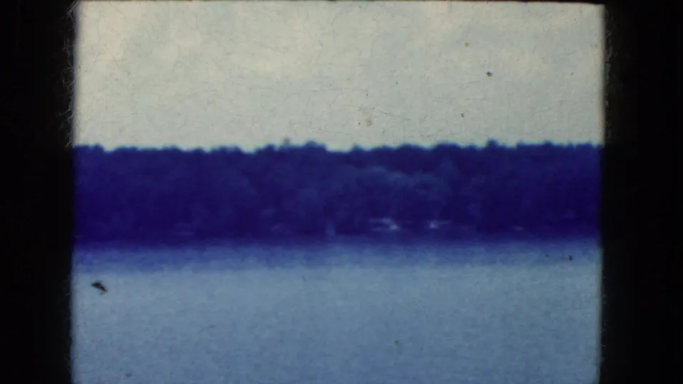 Blue-tinted 8mm frame of water and a far wooded shoreline near Niagara Falls, with soft focus, dust specks, and dark film edges.