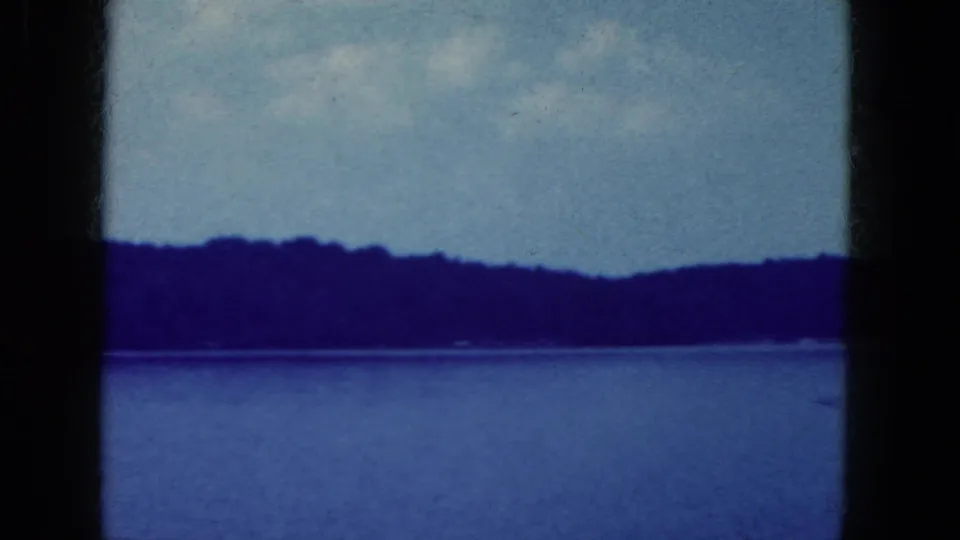 Blue-tinted 8mm landscape frame of calm water and distant wooded shore, supported by Niagara Falls, New York clip metadata.
