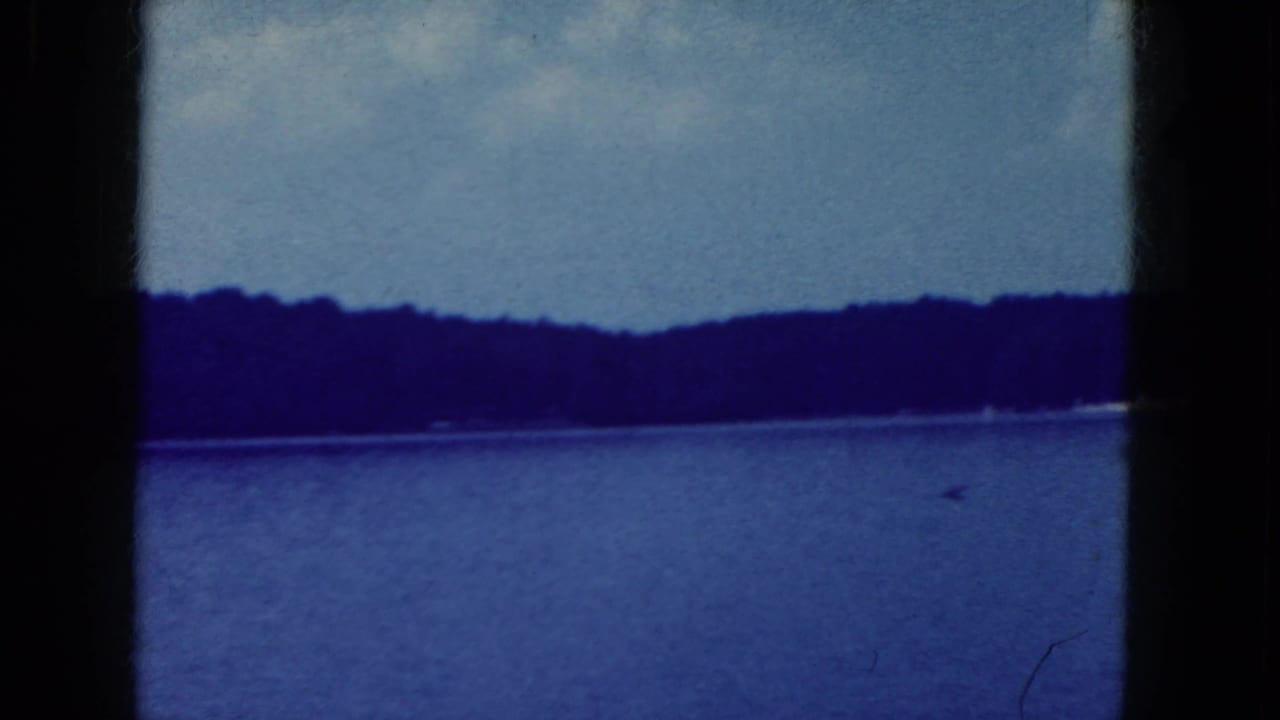 Blue-tinted lake view with distant tree-lined shore and dark film-frame borders.