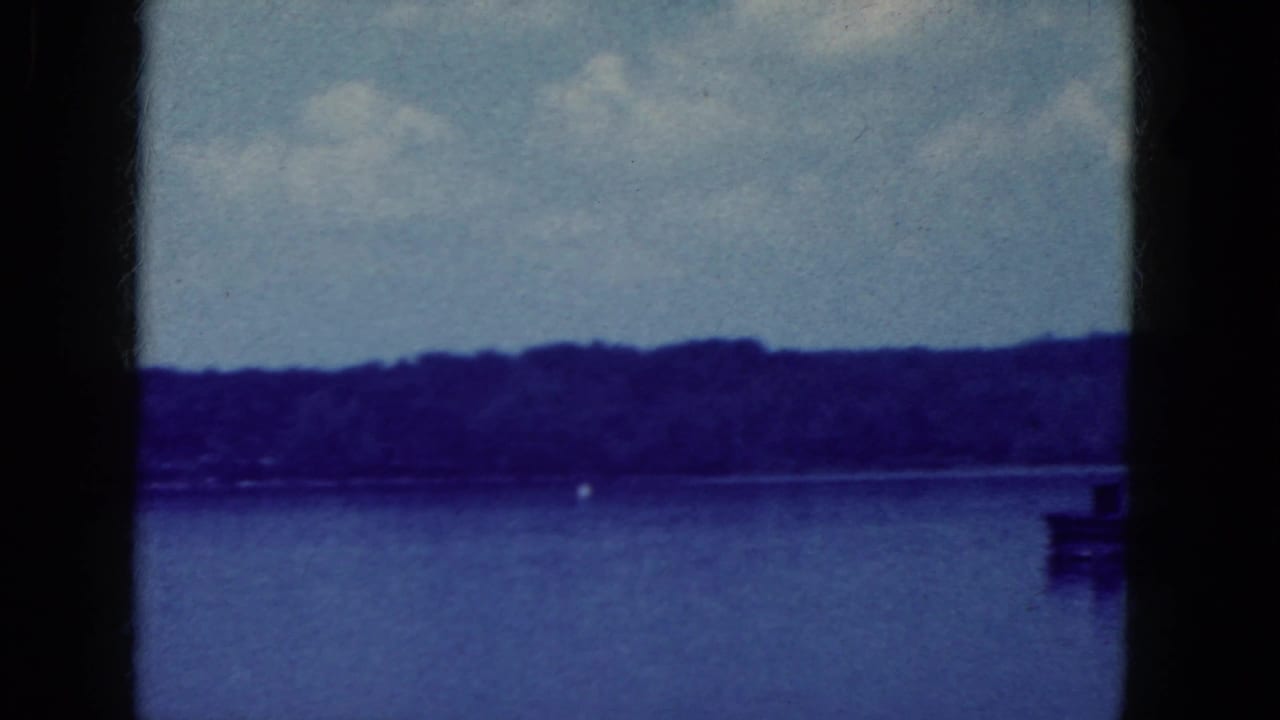 Lake and distant tree line seen through dark vertical film-gate divisions, with a small buoy on the water.