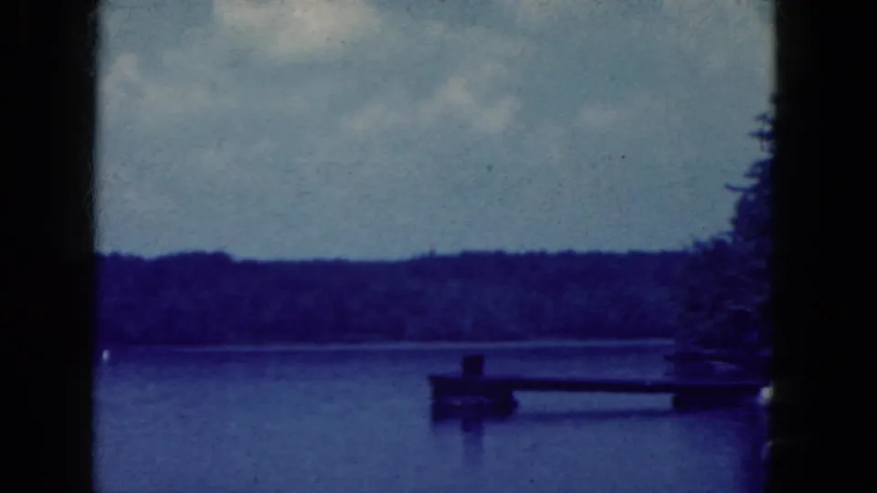 1964 Niagara Falls, New York home-movie frame showing a small dock, lakeside trees, calm water, and distant wooded shore.