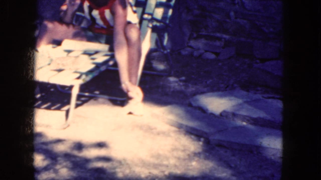 Woman in a striped swimsuit sits on a folding chair near a stone wall and reaches toward a squirrel.
