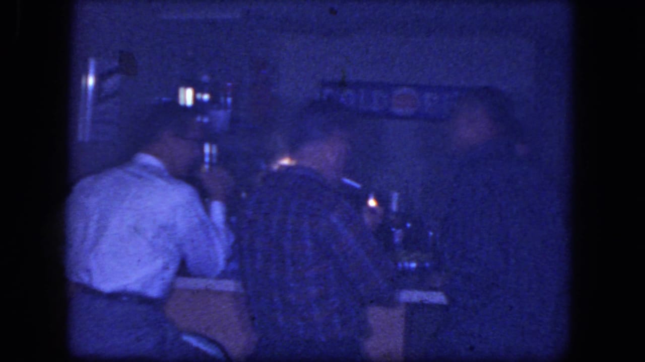 Men seated at a dim bar counter with wall signage behind them.