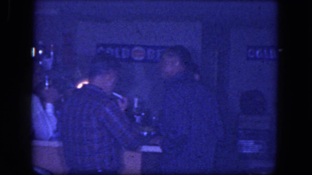 A man in a plaid shirt sits at a low-lit bar in the supplied 1964 Niagara Falls footage, with other adults nearby.