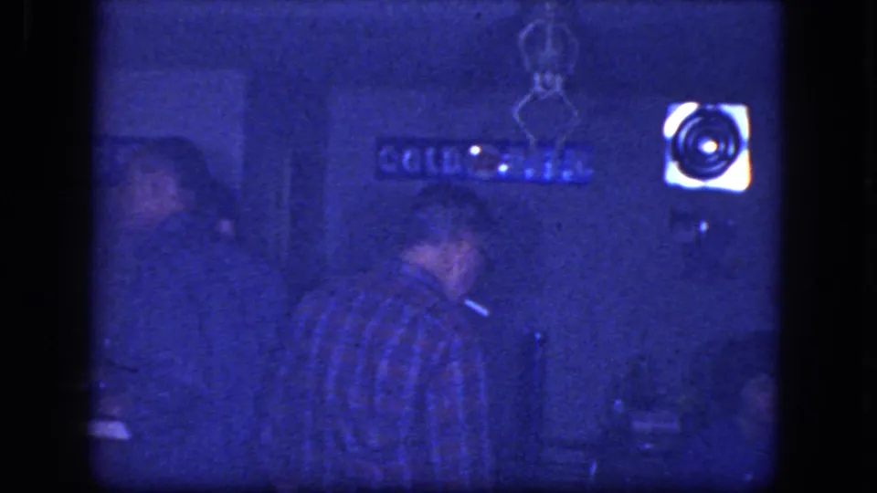 Men remain at the dim bar counter in the supplied Niagara Falls footage, with a bright wall light or sign visible to the right.