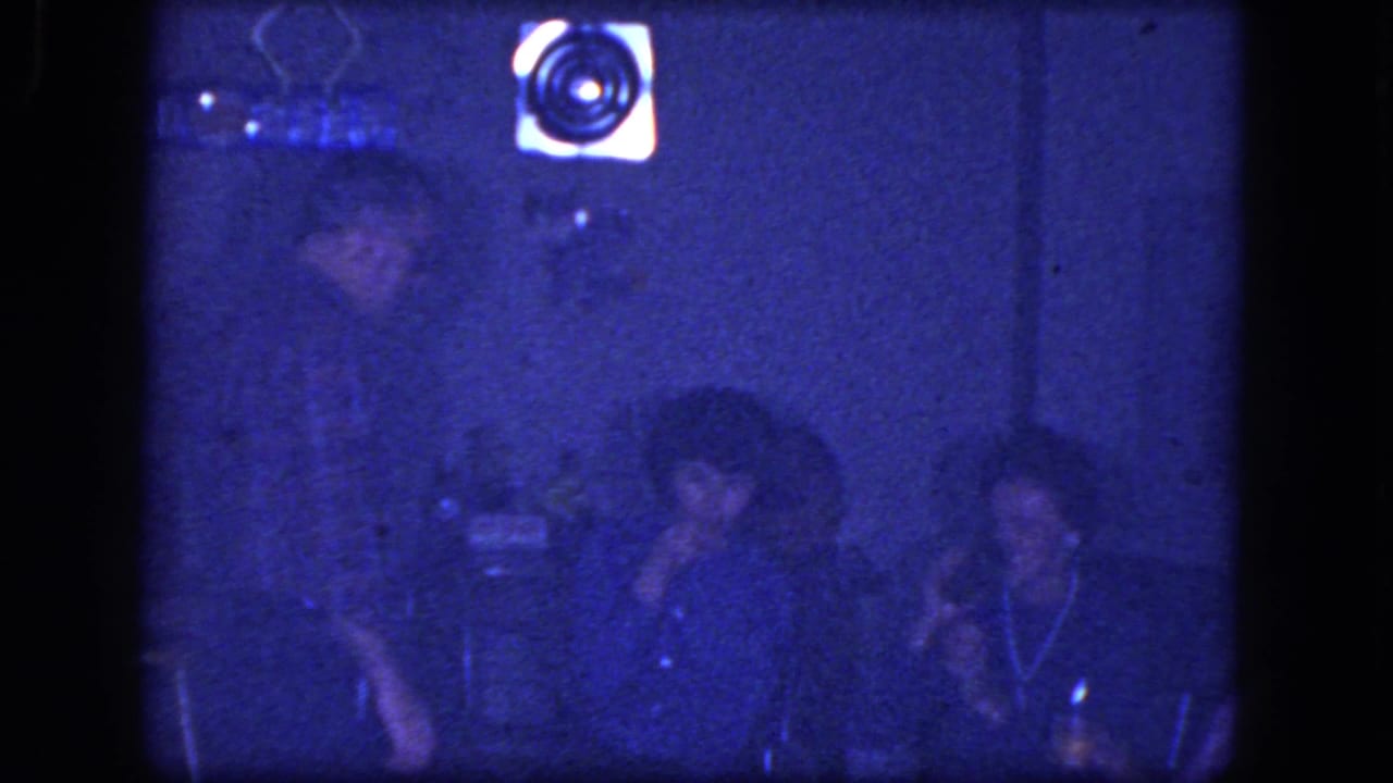 Adults sit together in a dark room, with one person holding a cigarette near their face.