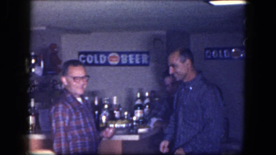 1964 Niagara Falls home-movie frame of men at a basement bar with visible bottles, signage, and private interior details.