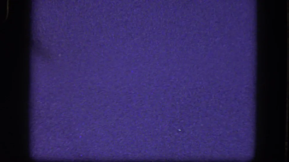 Mostly blank 1964 8mm frame with blue-purple cast, rounded film-gate corners, grain, and small dust marks.