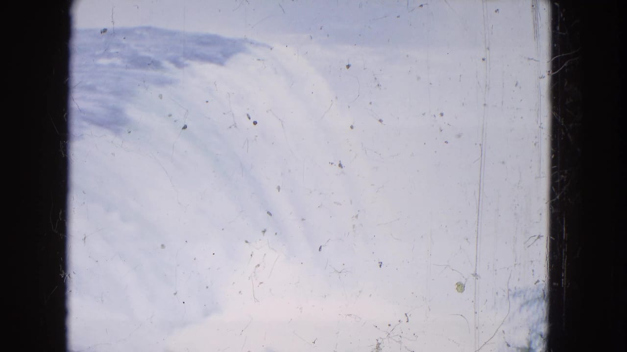 1964 8mm home-movie view of Niagara Falls from a distance, with pale sky, falling water, and visible film scratches.