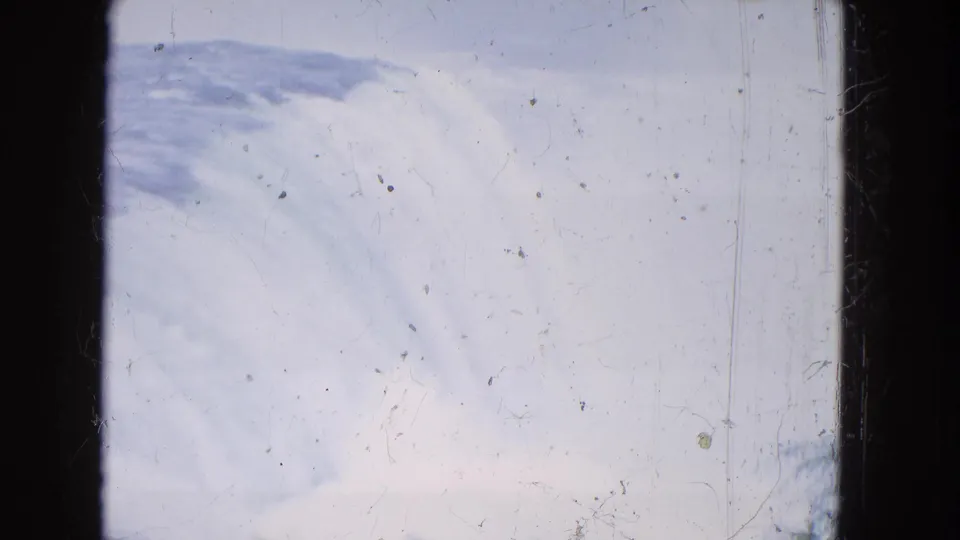 1964 8mm home-movie view of Niagara Falls from a distance, with pale sky, falling water, and visible film scratches.