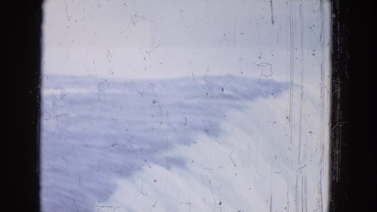 1964 Niagara Falls home-movie frame with a wide band of moving water, pale sky, dust, and scratches.