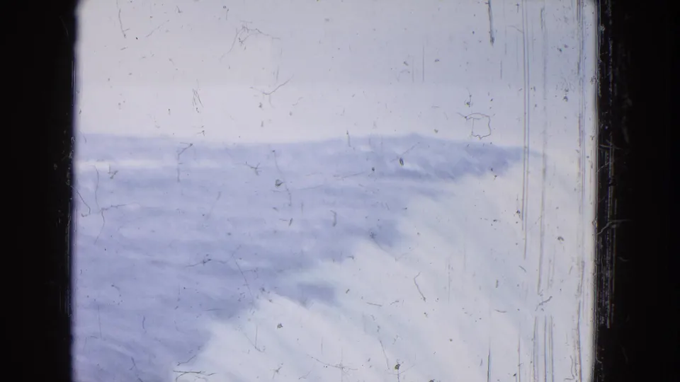 1964 Niagara Falls home-movie frame with a wide band of moving water, pale sky, dust, and scratches.