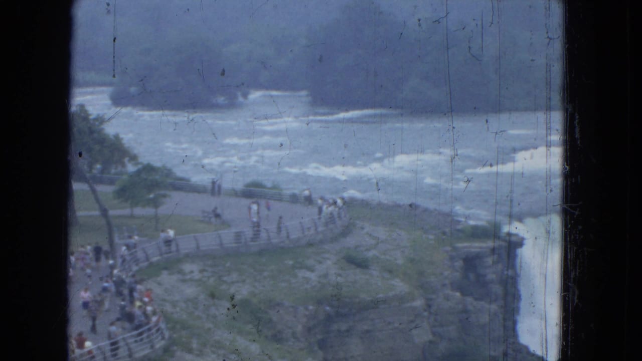 1964 8mm view of Niagara Falls from an overlook, with tourists by railings and white water beyond.