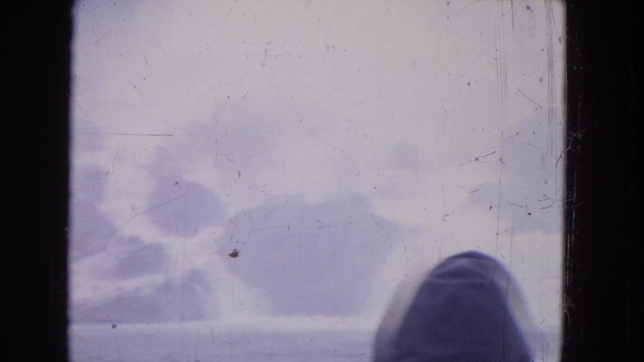 A hooded person appears at the lower right of a 1964 Niagara Falls 8mm frame with mist and storm clouds.