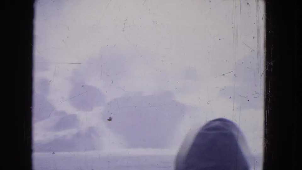 A hooded person appears at the lower right of a 1964 Niagara Falls 8mm frame with mist and storm clouds.