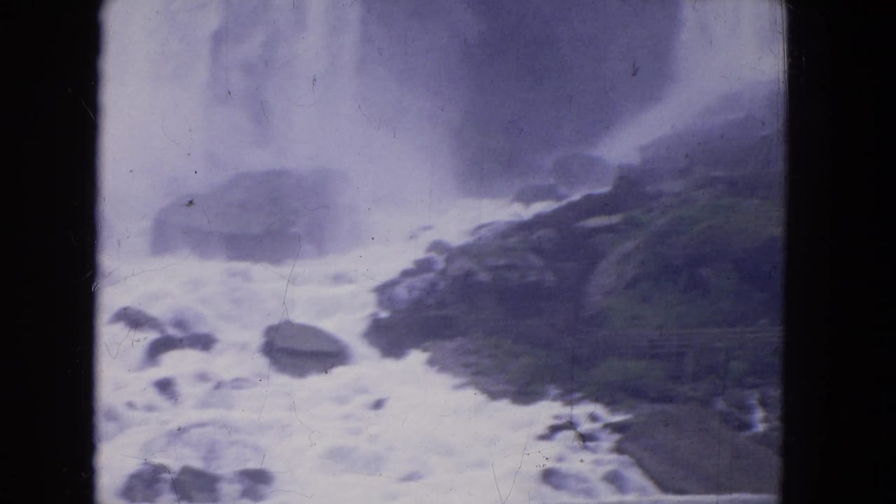 Water rushes around rocks below a misty waterfall edge.