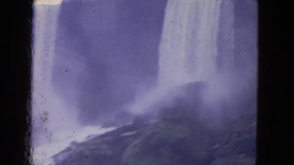 Visitor-shot 1964 Niagara Falls footage with a broad falling sheet of water, rocks below, heavy mist, and faded 8mm color.