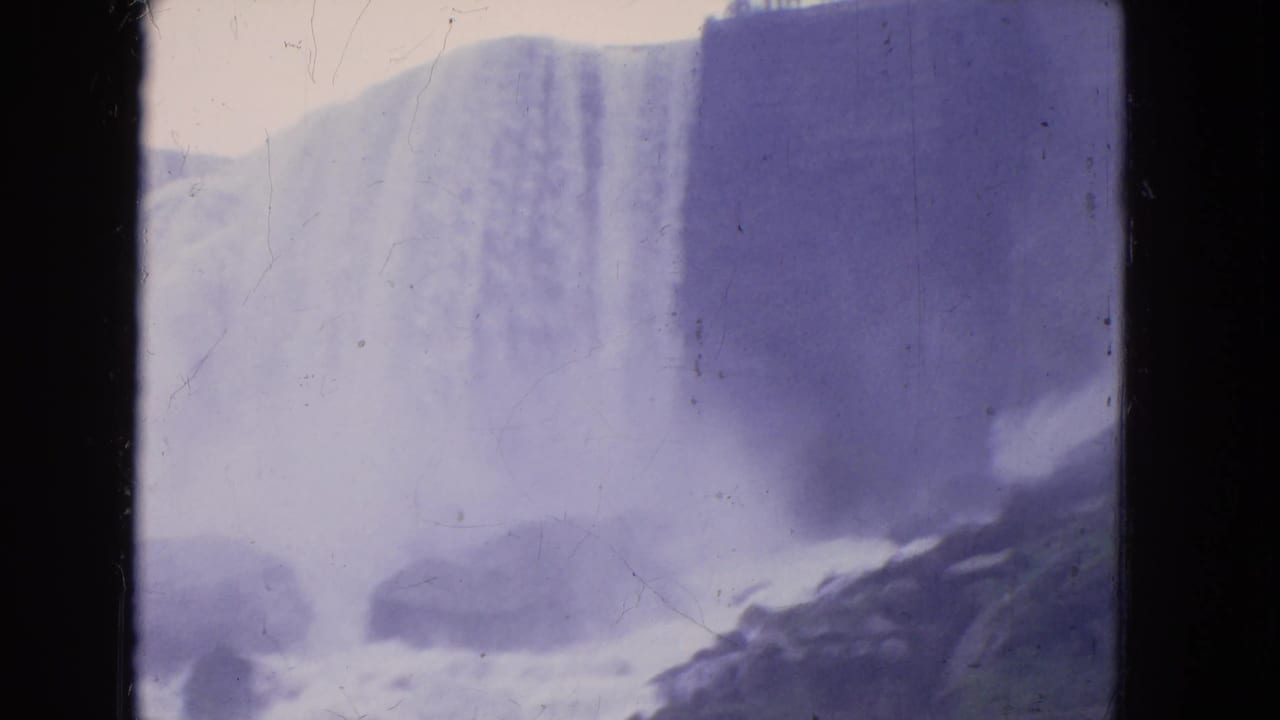 1964 8mm view of Niagara Falls water dropping over a broad ledge, with rocks below and heavy purple film cast.