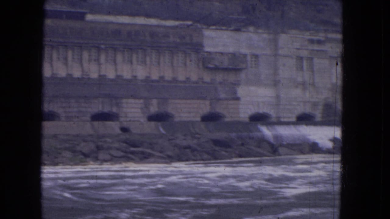 1964 8mm Niagara River boat view with rough water, stone embankment, arched openings, and a large masonry facade.