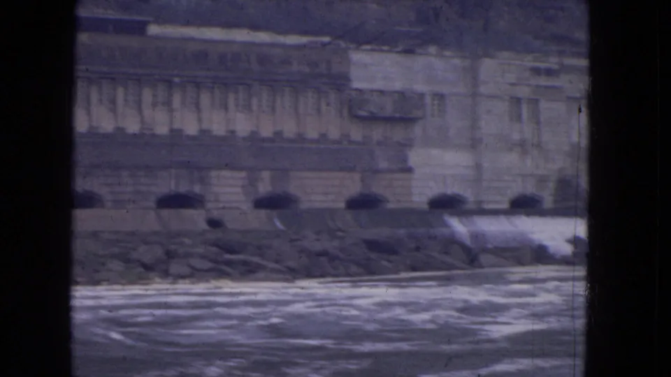 1964 8mm Niagara River boat view with rough water, stone embankment, arched openings, and a large masonry facade.