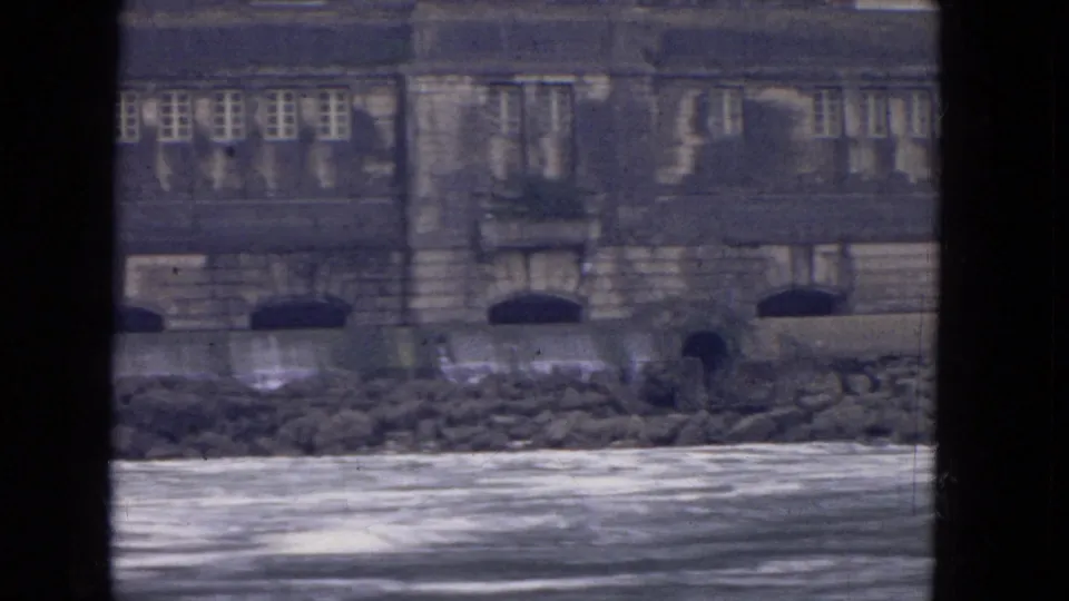 End frame of a 1964 Niagara River boat shot with choppy water and a weathered stone structure along the bank.