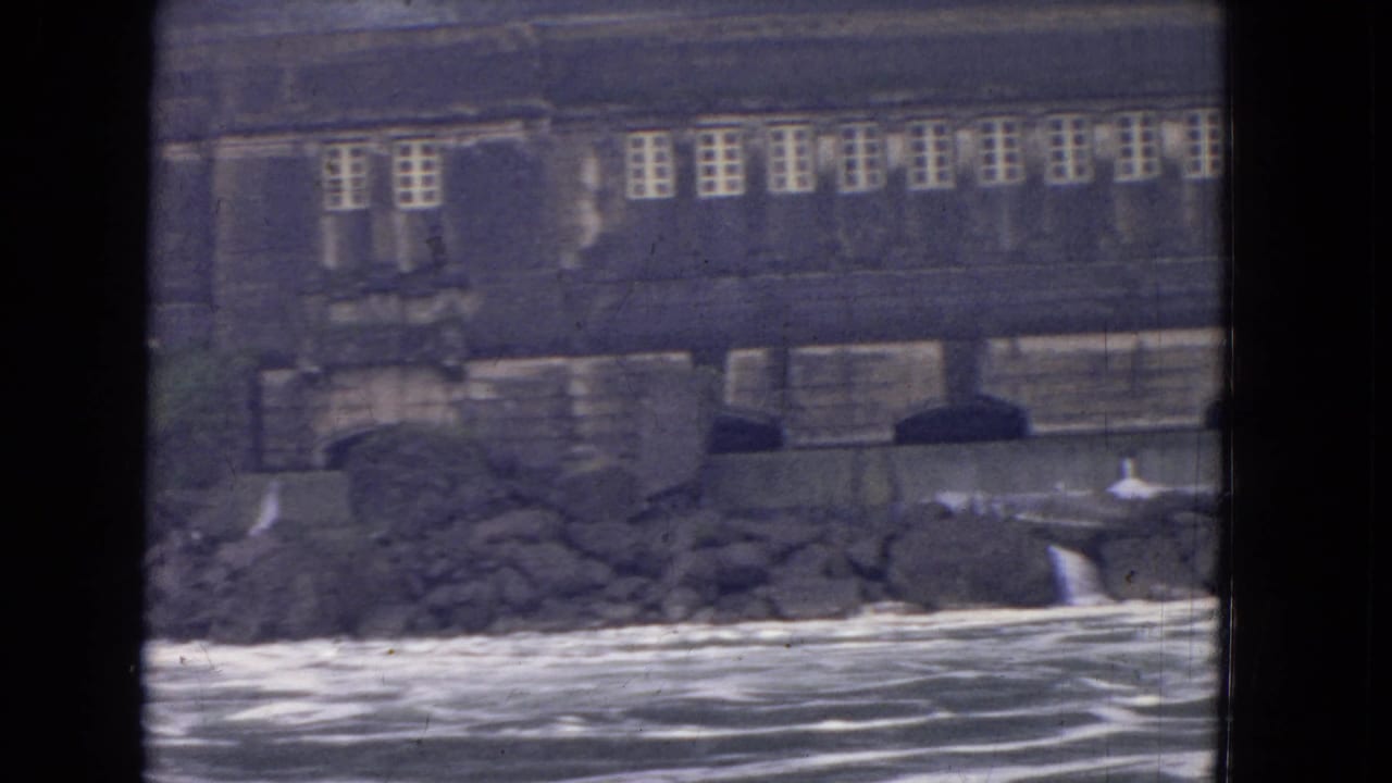 Stone riverside building with arched openings above a rocky bank and river.